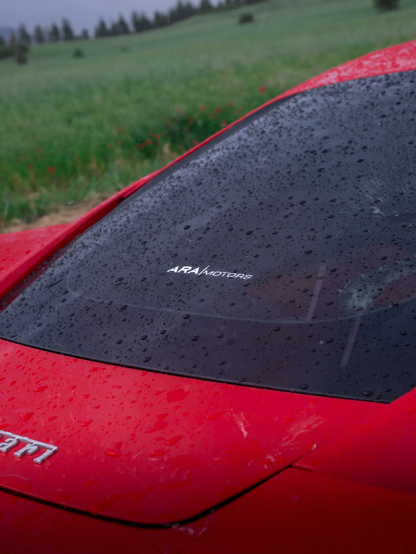 Ferrari ön camında yağmur damlaları arasından okunan Ara Motors yazısı